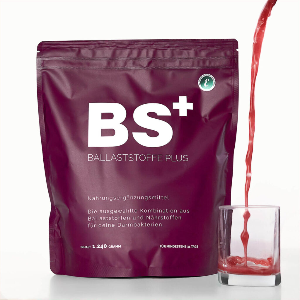 Produktverpackung von BS+ Ballaststoffe Plus mit einem roten Getränk, das daneben in ein Glas gegossen wird